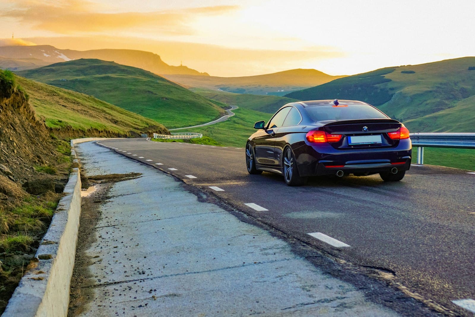 Dark blue sports sedan driving along a winding mountain road at sunset