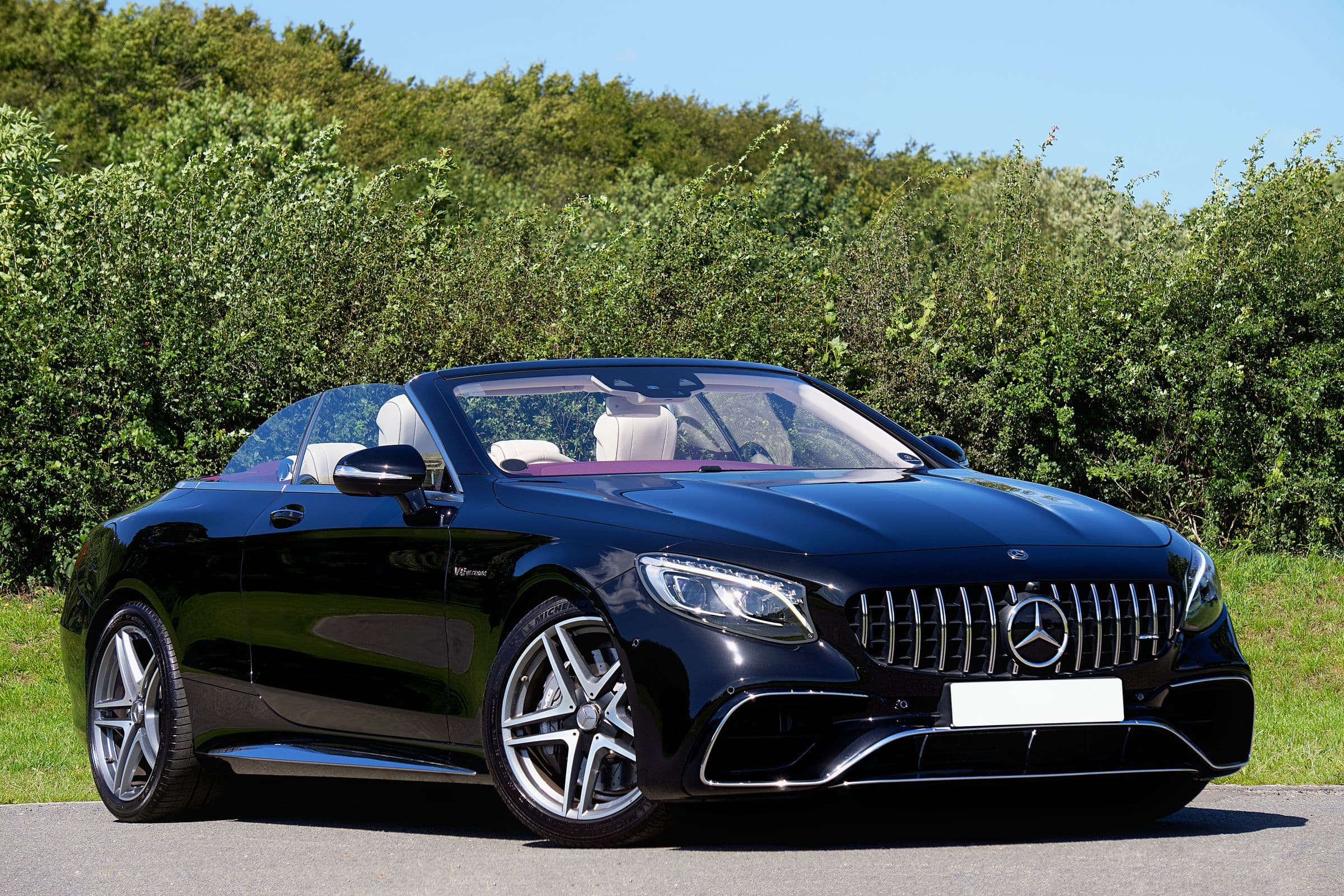 Black Mercedes-Benz S-Class convertible with the roof down, parked beside green hedges